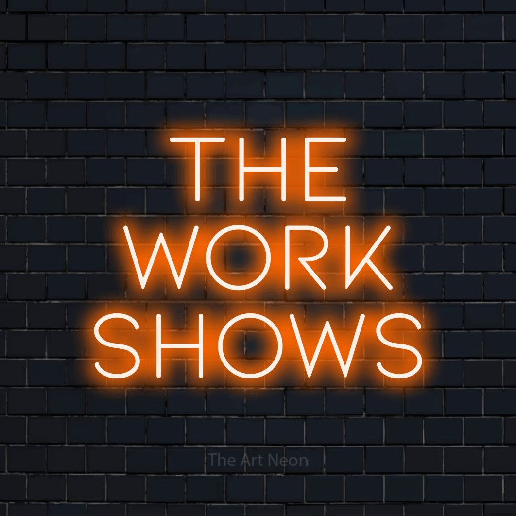 "The Work Shows" script-style LED neon sign on a black brick wall