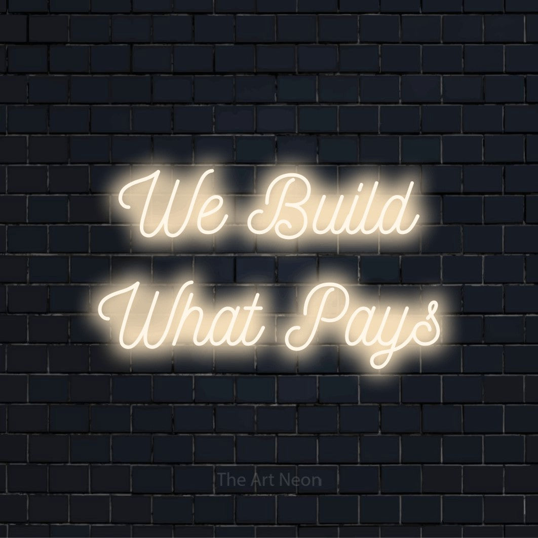 "We Build What Pays" script-style LED neon sign on a black brick wall