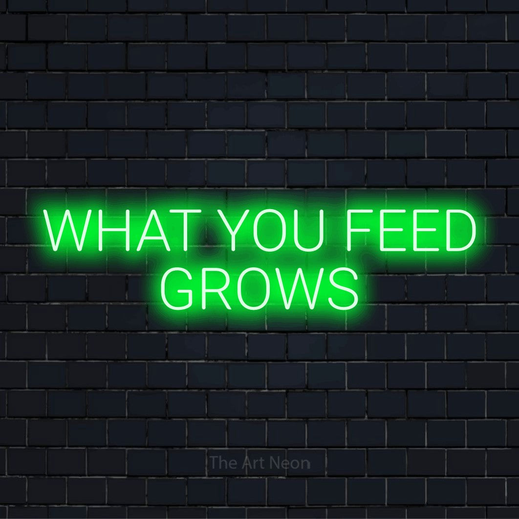 "What You Feed Grows" LED neon sign on a black brick wall