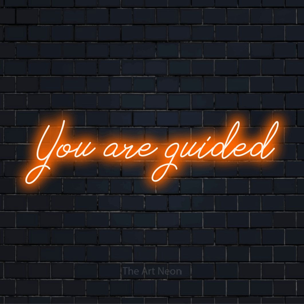 "You Are Guided" text design with neon effect on a black brick wall