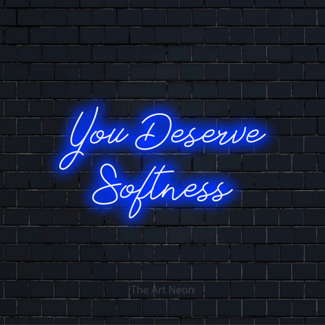 "You Deserve Softness" text design with neon effect on a black brick wall