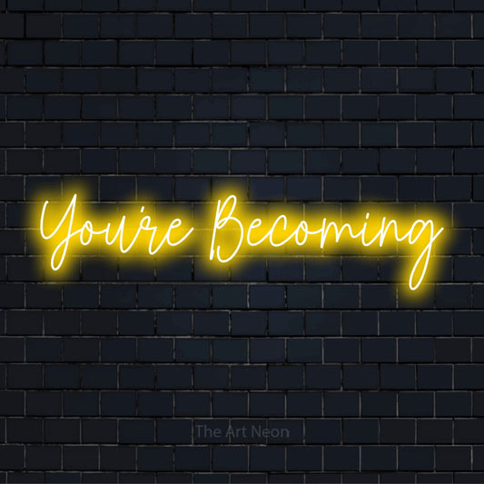 "You’re Becoming" glowing LED neon sign on a black brick wall