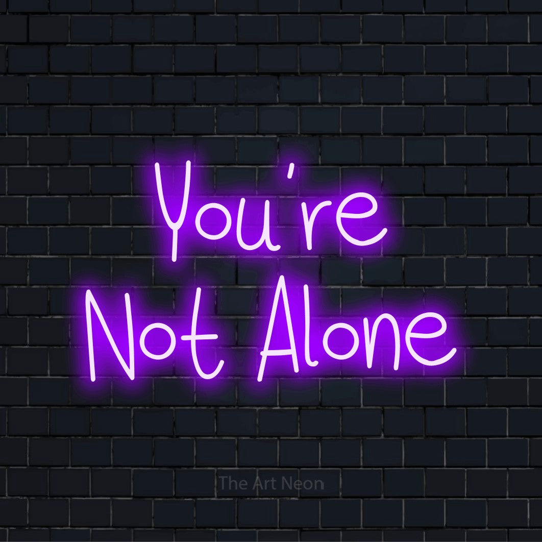 "You’re Not Alone" script-style LED neon sign on a black brick wall